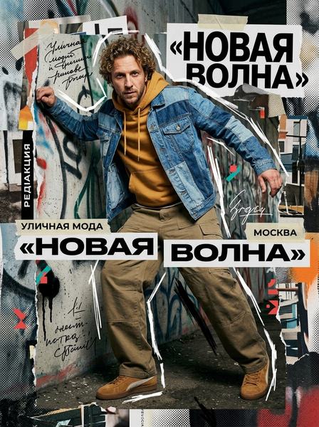 Кудрявый мужчина в джинсовой куртке и горчичном худи на фоне граффити и надписи «Новая волна»