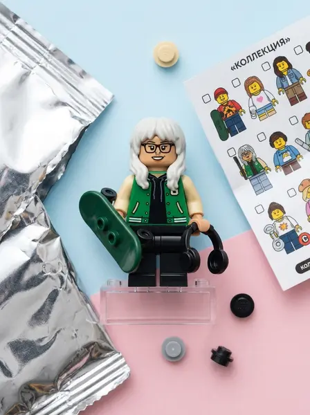 LEGO-минифигурка в очках и зелёном бомбере со скейтом рядом с фольгированным пакетиком и буклетом