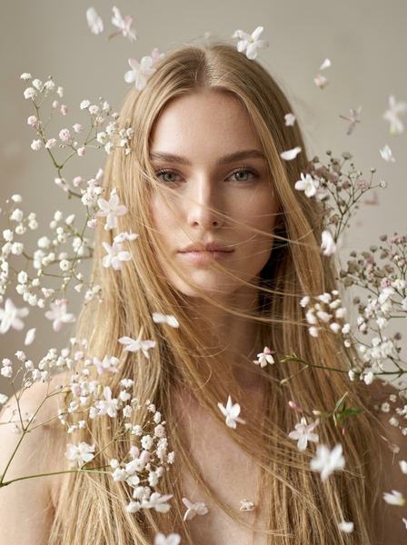 Девушка с развевающимися волосами в окружении летящих нежных цветов на бежевом фоне