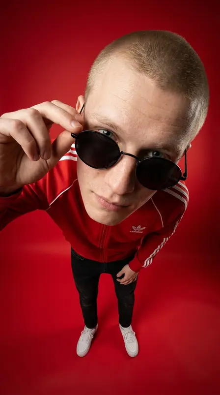 Парень в красной куртке Adidas и круглых очках снят сверху широкоугольным объективом на красном фоне