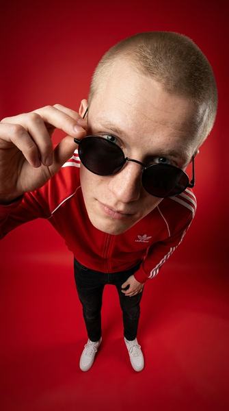 Парень в красной куртке Adidas и круглых очках снят сверху широкоугольным объективом на красном фоне