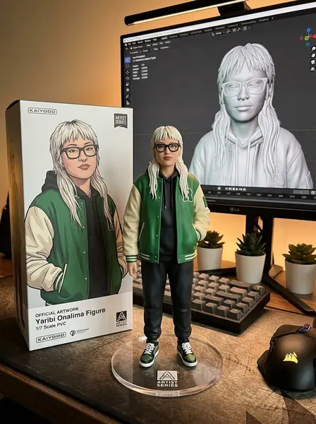 Фигурка девушки в очках и зелёном бомбере на столе у монитора с 3D-моделью и коробкой